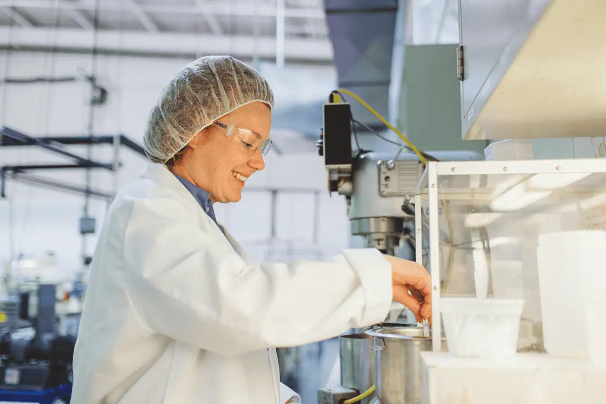 Scientist in lab coat smiling in industrial lab setting.
