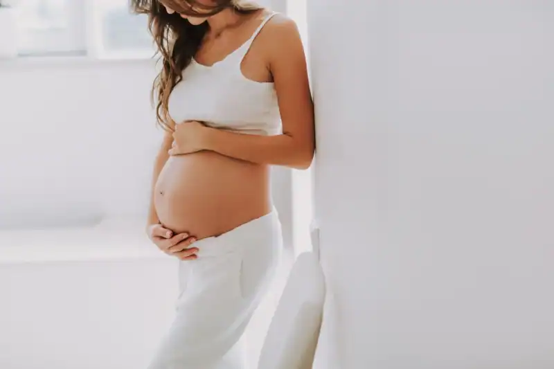 Woman in white holding her pregnant belly